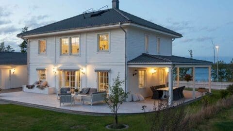 Weißes Holzhaus mit beleuchteten Räumen in Abendstimmung