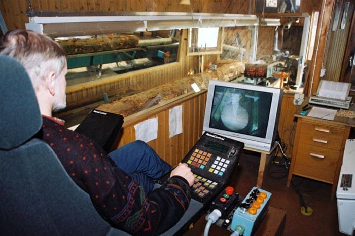 nachhaltigkeit bei eksjöhus: Arbeiter vor in holzverarbeitendem Betrieb Eksjöhus vor Bildschirmdarstellung eines Baumstamms