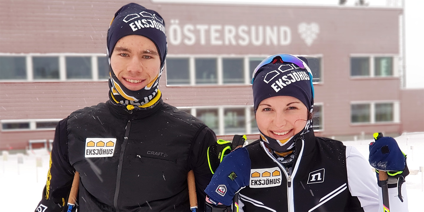 Schwedisches Wintersportlerpaar in Skikleidung steht vor Gebäude im Schnee