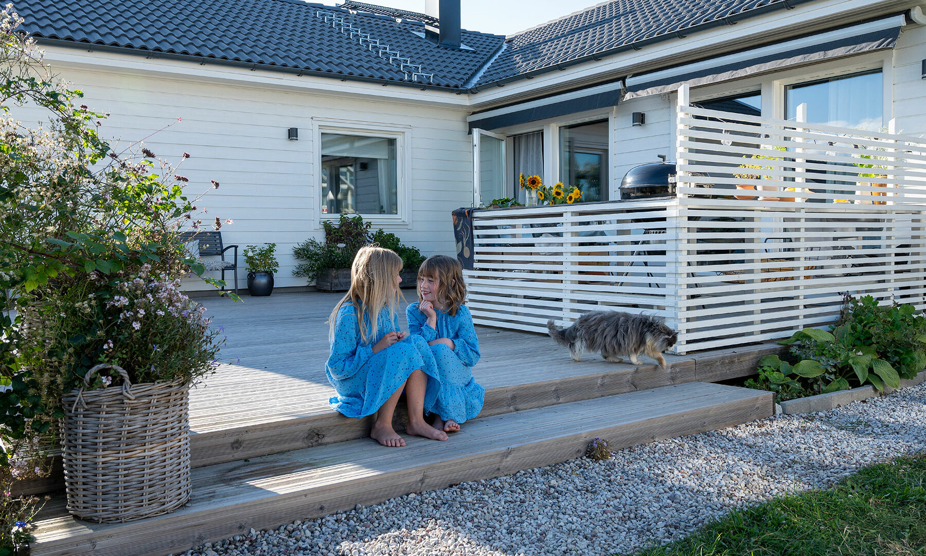 Mädchen in blauen Kleidern sitzen vor Haus von Eksjöhus