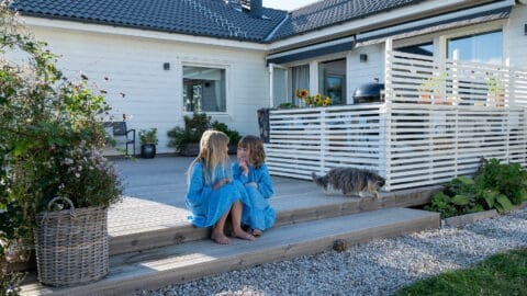 Mädchen in blauen Kleidern sitzen vor Haus von Eksjöhus